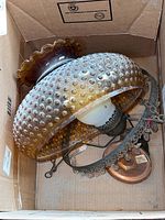 Top view of vintage hobnail amber glass hanging light fixture inside cardboard box, showing bulb, metal hanging hardware, and rounded flared scalloped top of glass shade.