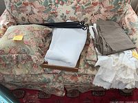 Floral patterned twin bedskirt and pillow on floral sofa along with folded linens and black iron rods