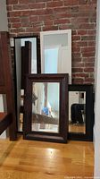 Four mirrors with frames leaned against a brick wall on wooden floor