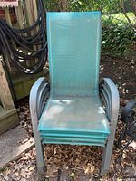 Front view of stacked five metal patio chairs with teal mesh seat and back, showing wear and rust