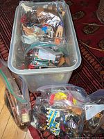 Large bin filled with Playmobil figures, animals, and accessories with zip bags on and around the bin showing assorted contents.