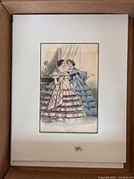 Matted vintage fashion print showing two women in mid-19th-century dresses with intricate details and colors, on cream mat with slight stain towards bottom.