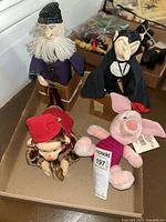 Four puppets/toys including a wizard, Dracula, mechanical monkey, and Piglet plush, displayed on a cardboard surface