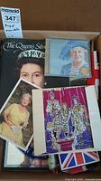 Photo of box containing royal family memorabilia including book, CD, framed print, photo, flag, paper doll book, and trivet