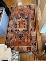 Top down view of the rectangular area rug showing full pattern and colors. Rug lies flat on wooden floor and has light fringe on shorter edges.