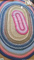 Large multicolor braided oval rug with blue, beige, green, pink and gray bands.
