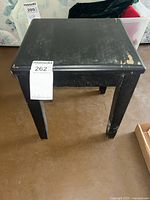 Front view of black painted wood side table showing paint loss on top corners and legs.
