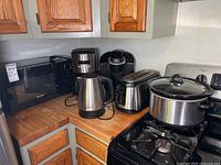 Corner countertop showing Kenmore microwave, Kenmore coffee maker, Hamilton Beach electric kettle, Keurig coffee maker, Hamilton Beach toaster, and Crock Pot slow cooker on a gas stove