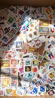 Photo showing a variety of used postage stamps scattered in a box, including colorful circus theme, fruit imagery, and flag designs mounted on paper backs.