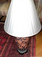 Full view of the lamp showing the white pleated fabric shade and porcelain floral base on a carpeted floor.