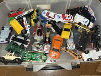Top view photo showing a plastic storage case filled with about 30 assorted toy cars including sedans, trucks, and race cars in various colors