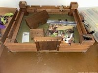 Full overview of wooden Fort Laramie toy model with bag of figurines inside on a wooden surface.