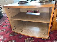 Front view of manufactured wood TV cabinet showing two shelves and an open back on a patterned carpet.