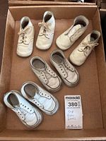 Four pairs of vintage leather baby shoes in a cardboard box, two pairs with laces and two without.