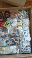 Overview of multiple plastic bags filled with vintage buttons and some belt buckles in a cardboard box