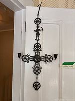 Full length photo of black metal candle holder in shape of a cross with three candle holders and a small human figure at the top.