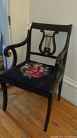 Full view of vintage wooden armchair with lyre back decorative backrest, curved armrests, and black embroidered floral seat cushion