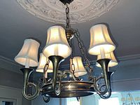 Full view of the chandelier showing five curved metal arms each with a white fabric shade and hanging from a chain.