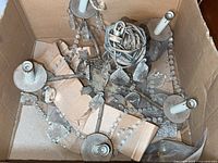 Chandelier components including five candle-style light holders, metal arms, wiring, and some chandelier crystals seen inside a cardboard box.
