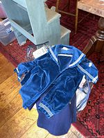 Photo of a navy blue velvet sailor suit jacket and matching pants laid on floor next to furniture, highlighting the sailor collar and fabric texture.