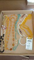 Overview of six beaded necklaces laid in a box showing colors and bead shapes