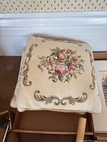 Top pillow is a vintage embroidered decorative pillow with a floral bouquet in the center surrounded by ornate embroidered scrollwork on a cream woven background.