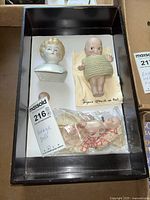 Photo showing two porcelain doll heads and a signed O'Neill baby doll wearing a knit outfit inside a box