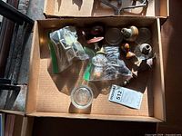 Multiple vintage glass and metal door knobs and parts in a cardboard box, showing variety of styles and materials.