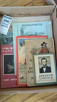 Box of vintage historical pamphlets including Abraham Lincoln, George Washington, Massachusetts, and Plymouth publications seen from an overhead angle.