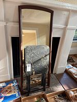 Full-length framed mirror and folding table leaning against fireplace.