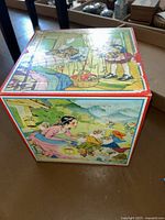 Photo of large nesting box showing a girl holding flowers in a room and a scene of a woman with dwarfs outside.