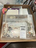 Plastic container with multiple paper doll figures and clothing cut-outs, visible vintage style dolls including full figures and separated clothing items.