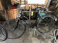 Side profile of vintage black Phillips bicycle including the frame, saddle, front basket, wheels with fenders, handlebar grips, and tire condition.