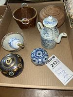 Overview of the lot showing all items including the mini teapot, two woven baskets, enameled brass jar, and porcelain box.
