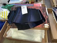 Box containing various fabric remnants including black silk, plaid, striped, and solid colored pieces