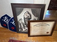 Wide shot of two framed items leaning against the wall with two Samuel Adams signs on the floor beside them.