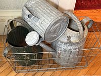 All three metal watering cans and wire basket shown from a diagonal side angle to display the lot contents and condition