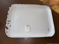 White enamel tray with visible black chipping and edge wear, rectangular with rounded edges.
