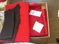 Box of folded red and black wool fabric remnants with some paper tags visible inside the box