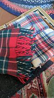 Three folded wool throw blankets in plaid patterns stacked together showing colors and fringe details.