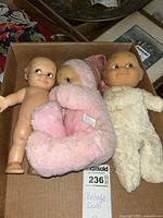 Three vintage Kewpie dolls in a box: one naked, one in pink sleeper, one in white fuzzy suit