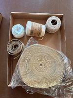 Top-down photo of a box containing a large coil of thick natural fiber webbing, a rolled narrow webbing strap, and three spools of twine of varying thicknesses.