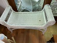 Top-down view of white wicker bench showing woven seat and curved armrests.