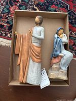 Photo showing both Mary holding baby Jesus seated figurine and Joseph standing figurine with staff inside a cardboard box on a carpet.