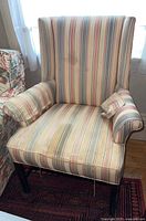 Front view of striped upholstered wingback chair showing vertical stripes upholstery, wooden legs, and visible stain on backrest.