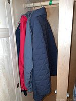 Three jackets in closet including red, gray, and navy quilted jacket, showing the variety in styles and colors in the lot.