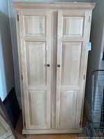 Front view of the wooden wardrobe showing two paneled doors with round knobs, natural unfinished wood.
