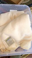 Plastic bin containing at least one folded cream or ivory colored wool blanket with Faribault label visible, blankets appear soft and clean.