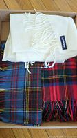 Photo showing three wool scarves: a white scarf with fringes and 'Land's End' label on top of two red and blue tartan scarves.