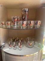 Front view of glassware pieces including shaker and glasses with pheasant decoration inside cabinet